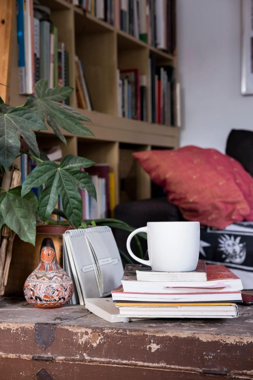 Weisse Tasse auf einem Bücherstapel vor einem gefüllten Bücherregal