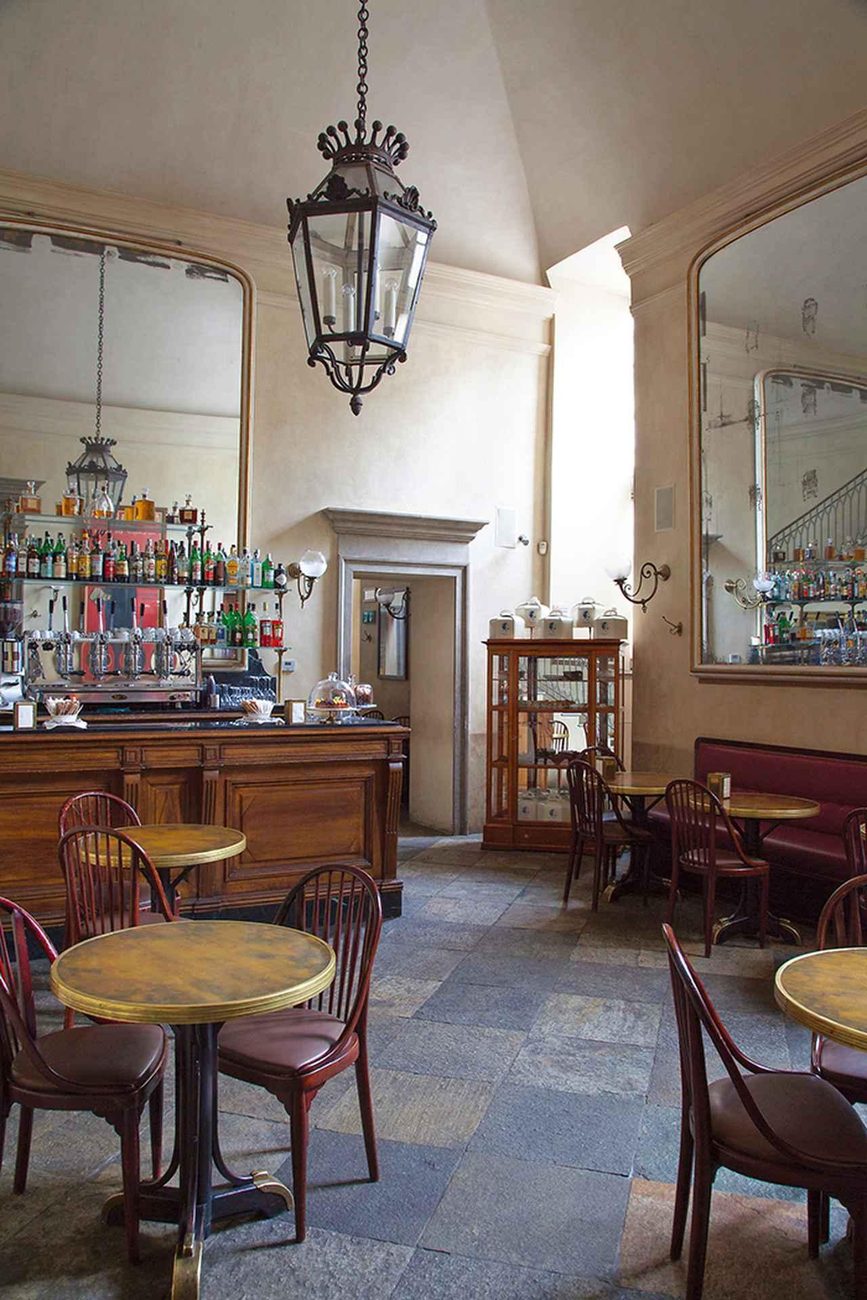 Innenraum einer italienischen Bar mit Marmortischen, Bugholzstühlen und Messinglampe