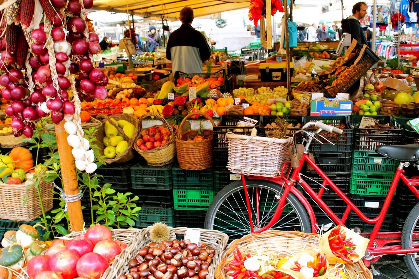Italienischer Marktstand mit Obst und Gemüse, davor ein rotes Fahrrad