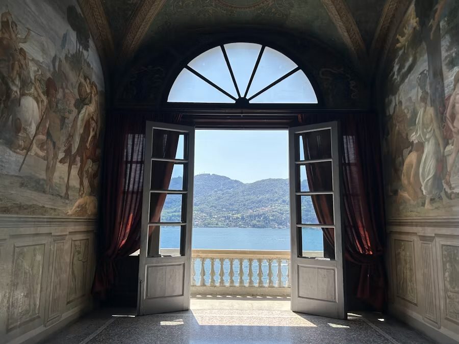 Offene Flügeltür eines freskierten Saals mit Blick auf einen oberitalienischen See